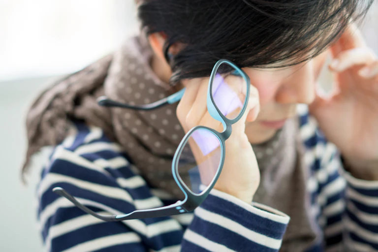 Woman holding glasses while holding side of head