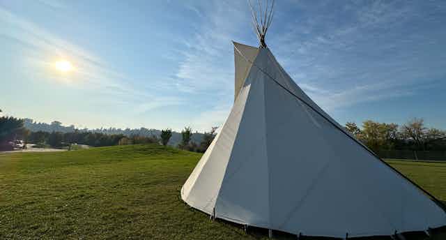 A teepee seen on green grass against a big sky.