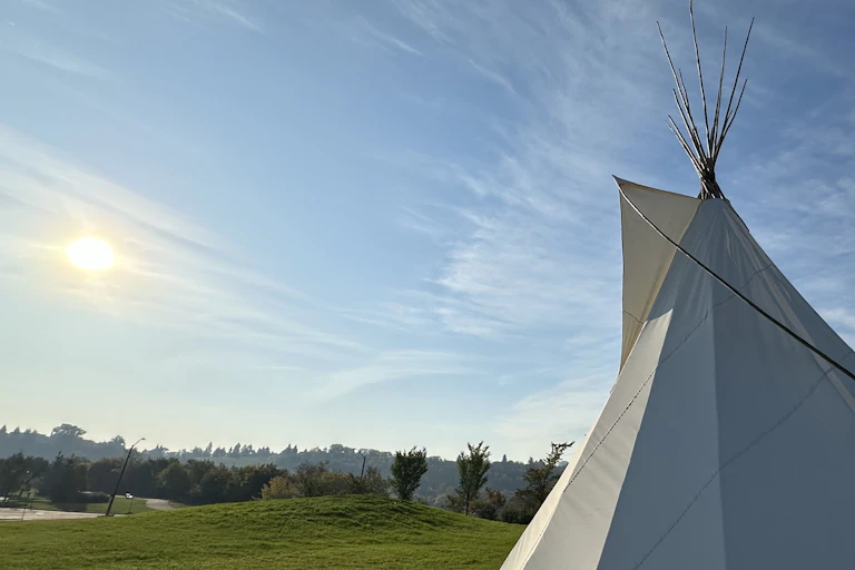 A teepee seen on green grass against a big sky.
