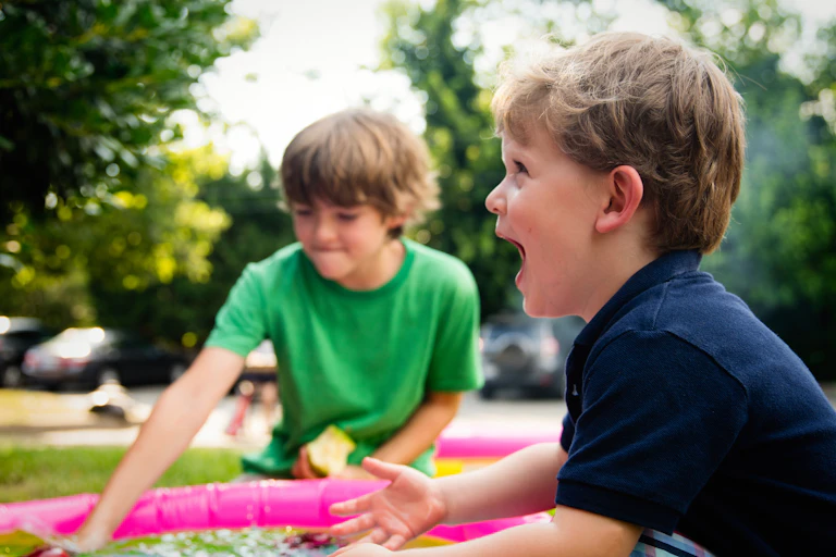 Two young boys put their hands in water. One shouts, then other looks amused.