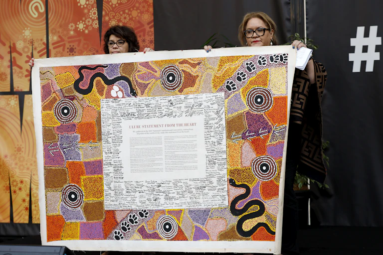 Two women holsing up the Uluru Statement