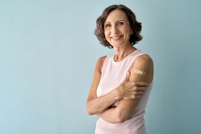 Older smiling woman clutching forearm, with bandaid over upper arm