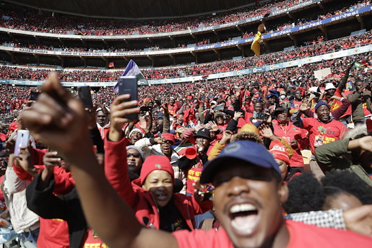 Thousands of people, many wearing red, cheer at a stadium.