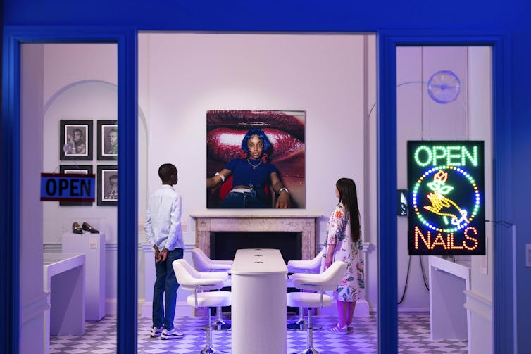 A young man and woman stand in an installation that looks like a nail salon.