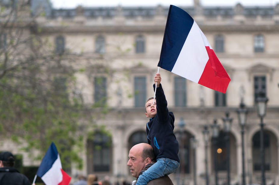 A child on a man's shoulders waves a French flag. 
