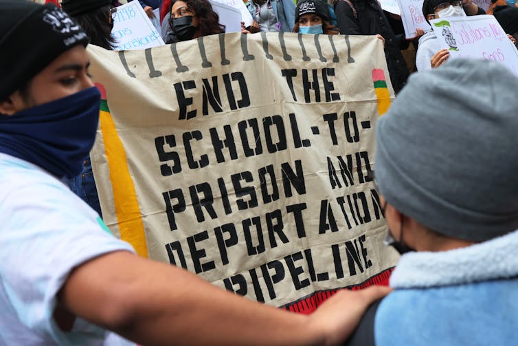 Young person at rally holds sign that says 'End the school to prison and deportatation pipeline'