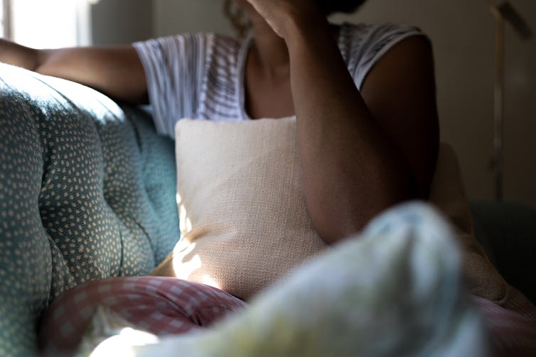 A woman looks to be crying on her couch. Her face is obscured.