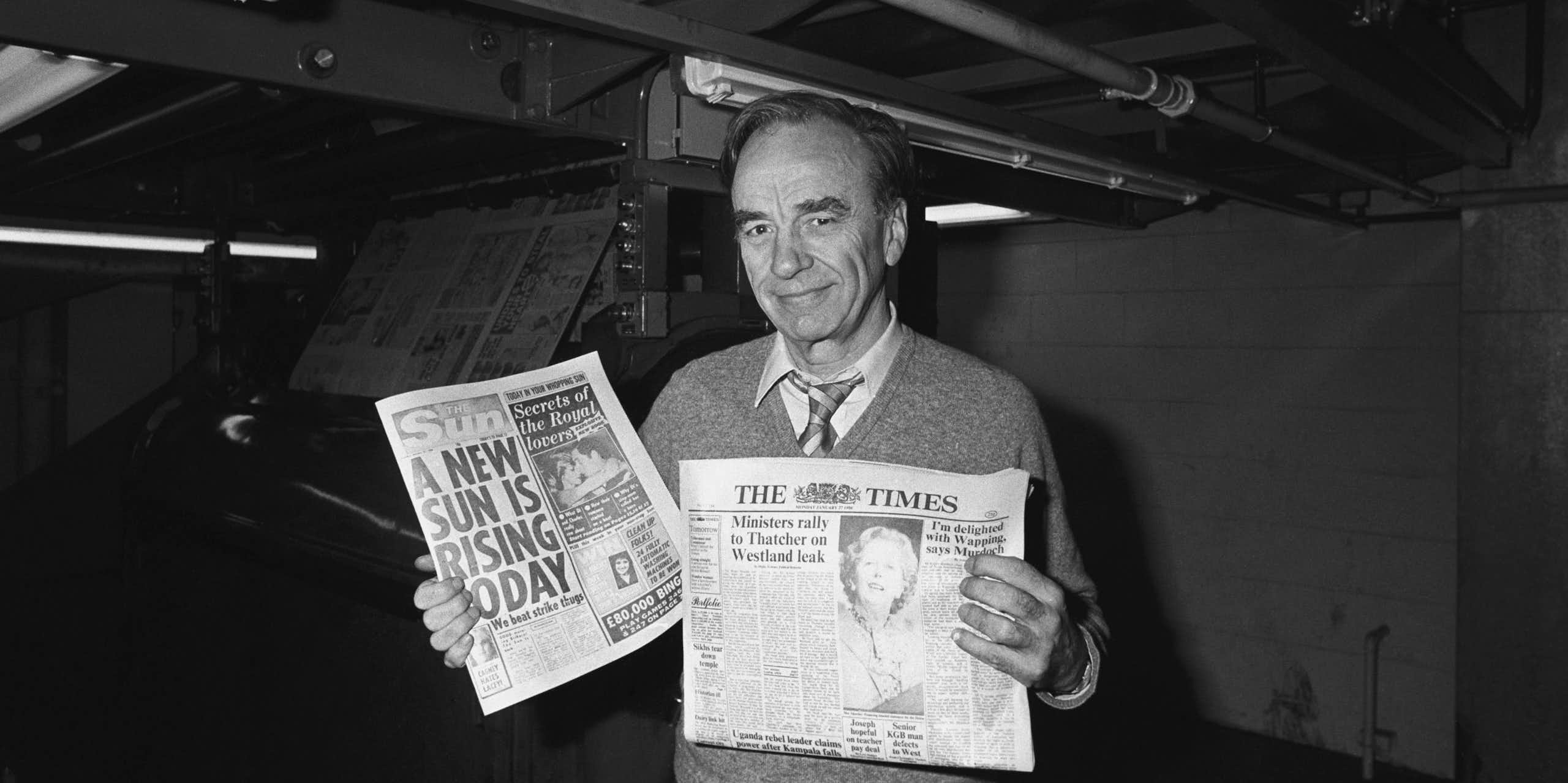 Rupert Murdoch holding newspapers at a print site in 1986.