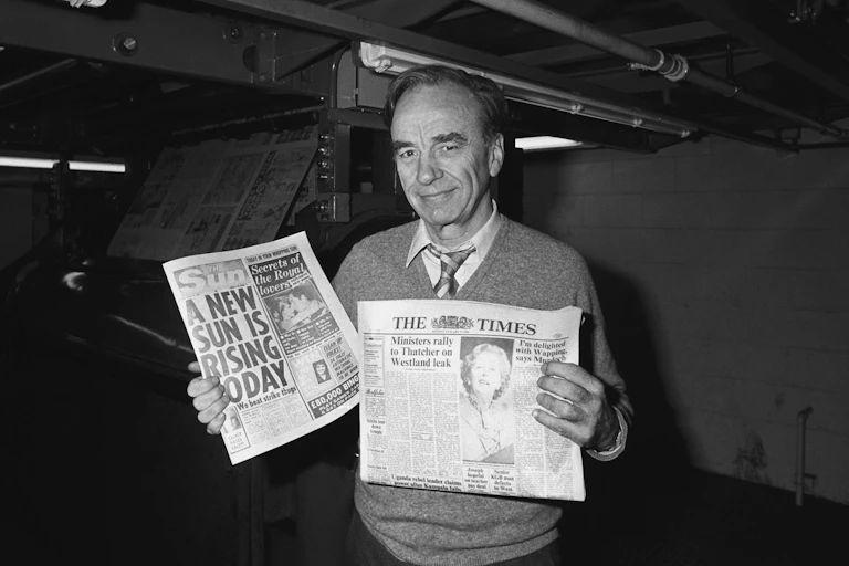 Rupert Murdoch holding newspapers at a print site in 1986.