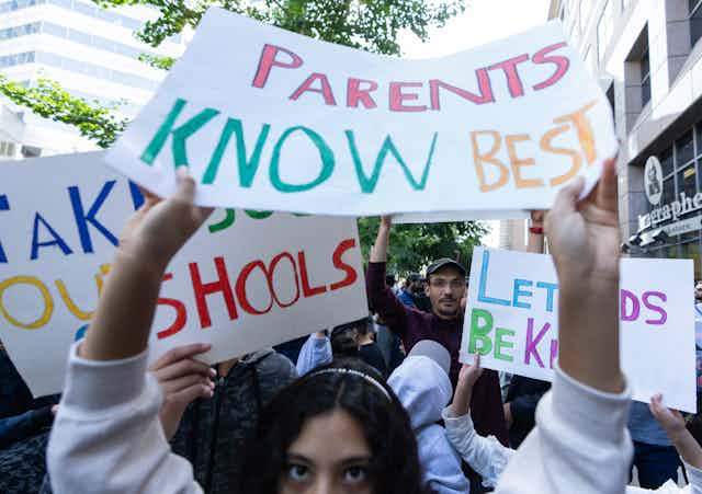 A dark-haired woman holds up a sign that reads Parents Know Best.