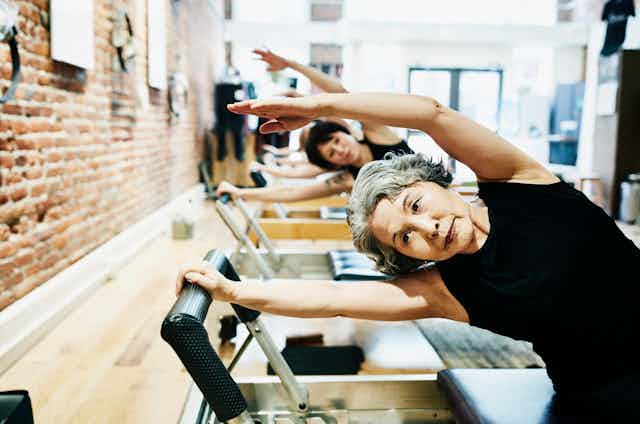 Mature women doing exercises on pilates equipment in a gym.