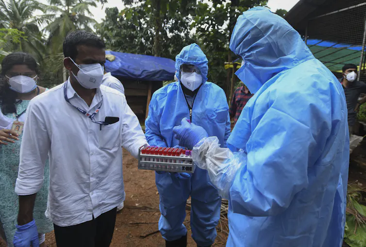 Três homens com vestes anticontaminantes examinam vidros com sangue