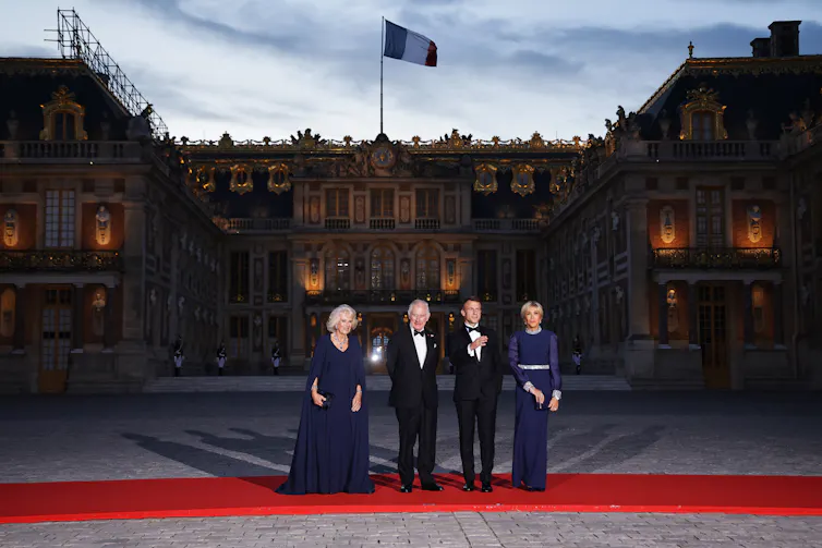 Queen Camilla, King Charles, Emmanuel Macron and Brigitte Macron standing on a red carpet in black tie.