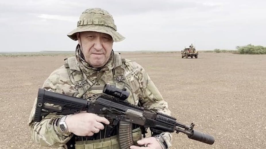Un homme en tenue de camouflage militaire pose avec un fusil automatique.