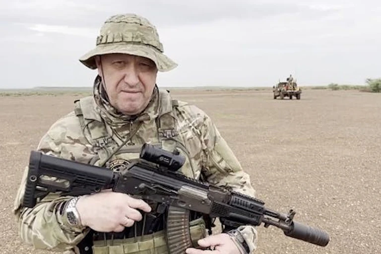 Un homme en tenue de camouflage militaire pose avec un fusil automatique.