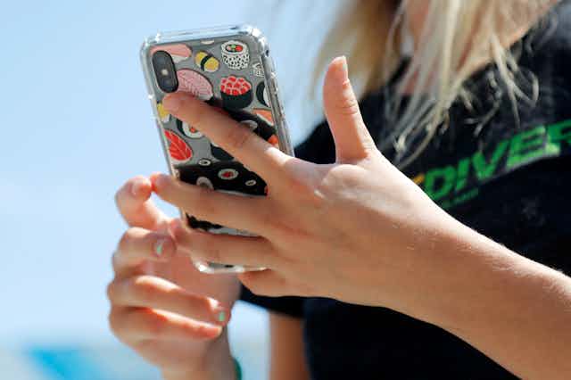 A pair of hands with small dabs of nail polish hold a smart phone that is covered with stickers depicting sushi items