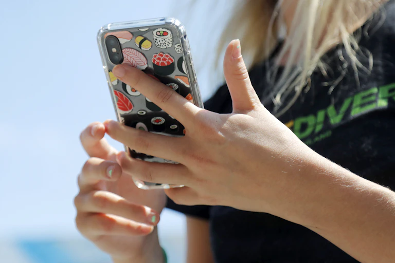 A pair of hands with small dabs of nail polish hold a smart phone that is covered with stickers depicting sushi items