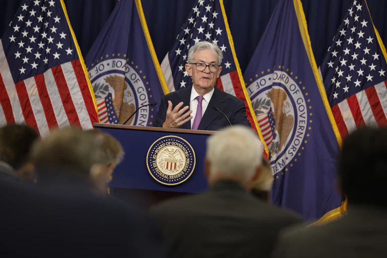 Jerome Powell, the chairman of the Federal Reserve, speaks to reporters. He is standing behind a lectern and in front of several American flags.