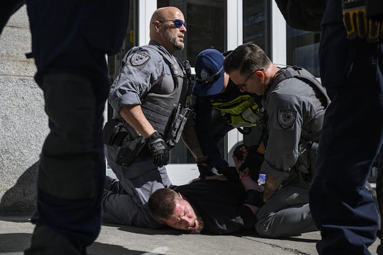 A man yells on the ground as police apprehend him.