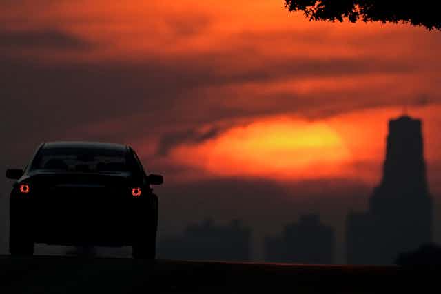A car drives towards the setting sun lighting up smoke from wildfires