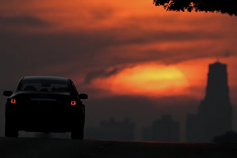 A car drives towards the setting sun lighting up smoke from wildfires
