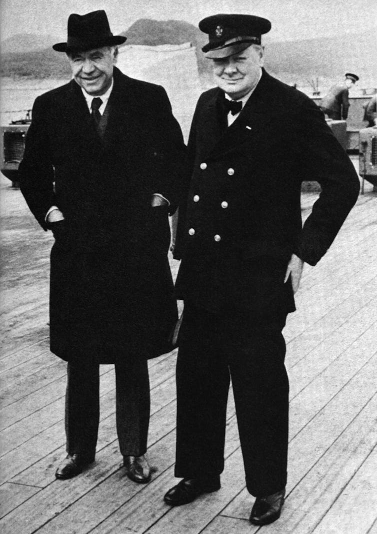 Winston Churchill stands with another man on the deck of a ship.