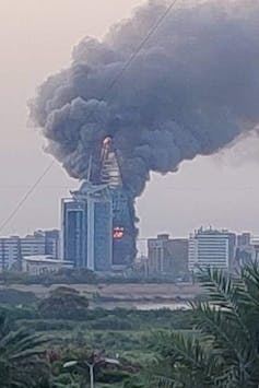 A cityscape with a skyscraper burning, black smoke billowing into the sky.