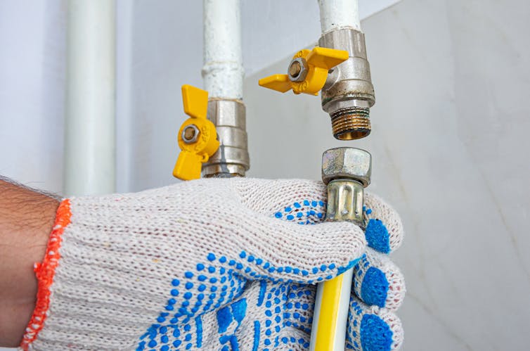 A gloved hand detaching a hose from a metal valve.