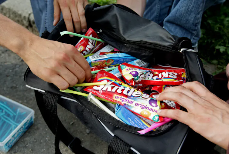 A collection of candies seen inside a backpack with hands reaching in.