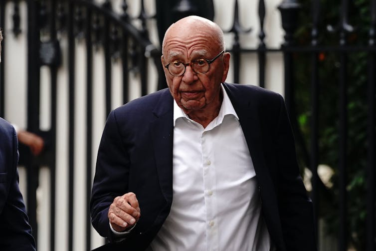 Rupert Murdoch wears a dark shit and walks in a street.