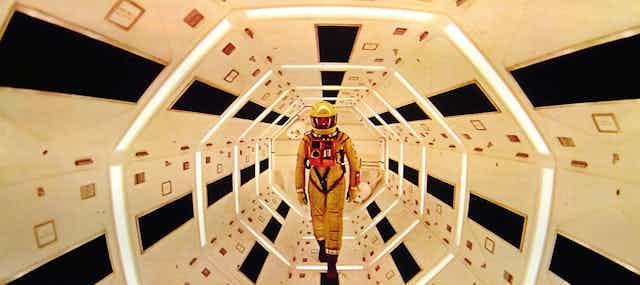 An astronaut in a yellow helmet stands within a futuristic white spaceship.
