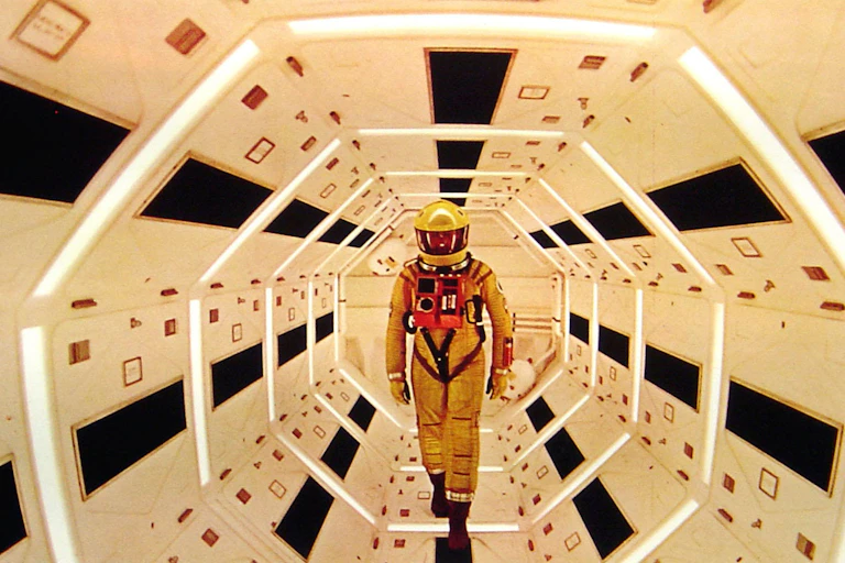 An astronaut in a yellow helmet stands within a futuristic white spaceship.
