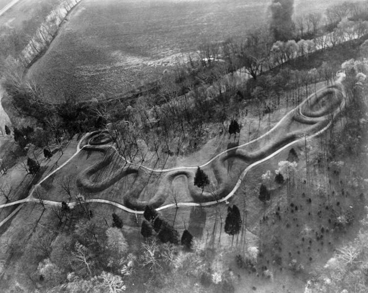 An aerial view of a mound shaped like a long snake holding an egg in its jaws.