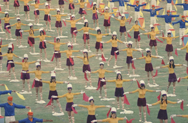 Women dance in formation wearing short skirts and carrying red ribbons.