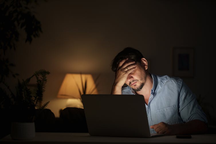 A man sitting at a table in a dimly lit room rests his head against his hand