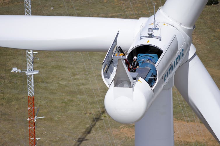 A worker stands in the nacelle of a wind turbine far above the ground.