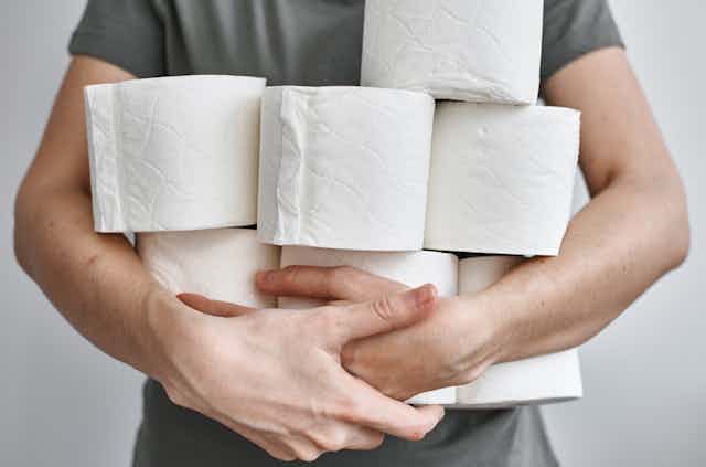 A man holds several rolls of loo paper.