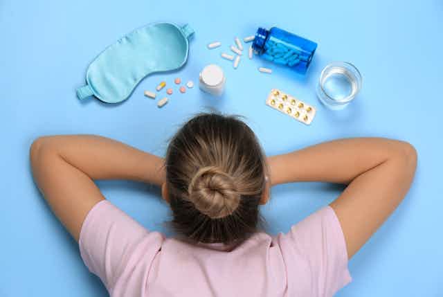 Young woman lying on front looking at pills, eye mask