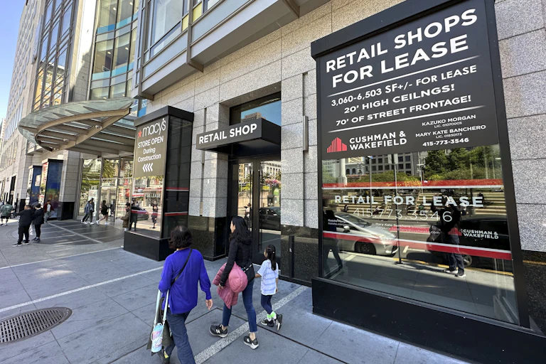 A few shoppers walk past a large downtown shopping mall advertising thousands of square feet of space for lease