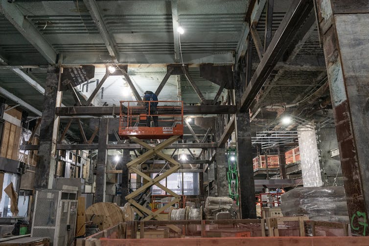 A construction worker on a movable scaffold in a gutted office building.