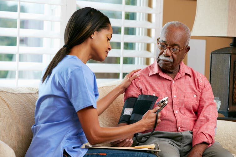 A nurse taking a man's blood pressure on a sofa