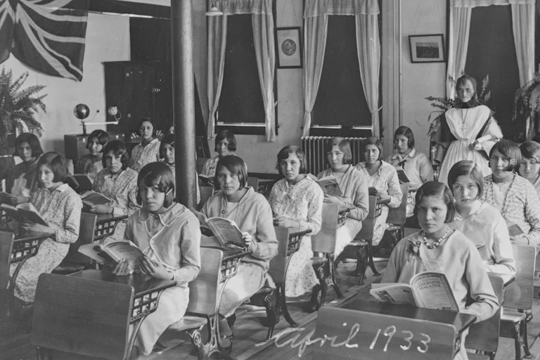 Black and white photo showing 1930s classroom of Indigenous adolescent girls sitting in rows of desks.