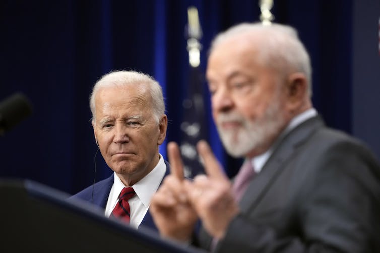 O presidente americano Biden presta atenção ao que diz o presidente Lula, que aponta os dedos indicadores para o alto