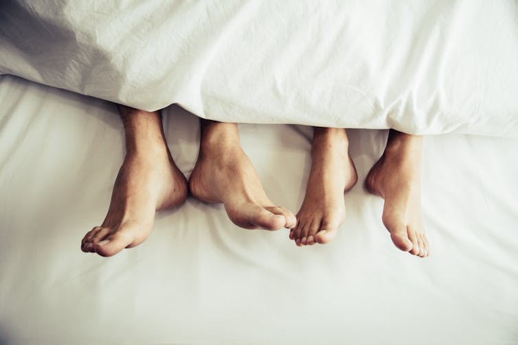 Two pairs of feet on a bed.