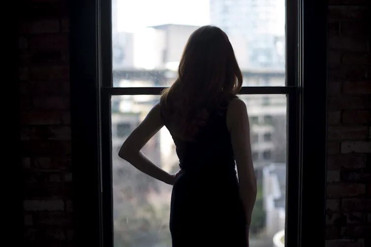 A woman wearing a black dress looks out of a window.
