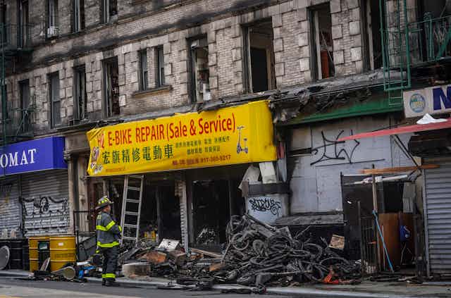 A fireman outside a charred storefront advertising e-bikes in English and Chinese