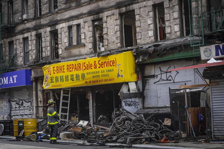 A fireman outside a charred storefront advertising e-bikes in English and Chinese