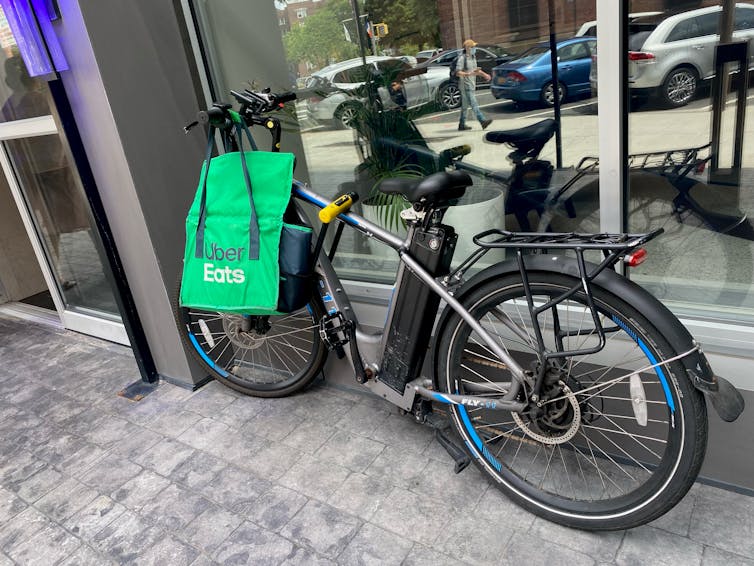Un vélo électrique avec un sac Uber Eats accroché au guidon à côté d’un bâtiment.