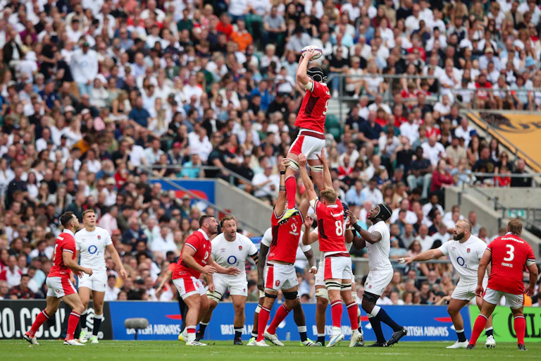 Un groupe de rugbymen en rouge hisse un joueur au-dessus d'un groupe de rugbymen en blanc.