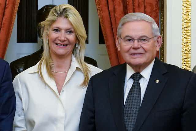 A smiling woman with dyed blonde hair standing next to a gray-haired man in a suit and tie.